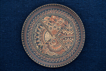 Decorative ceramic plate with black and golden colors, painted plate on the background of blue fabric, dot painting