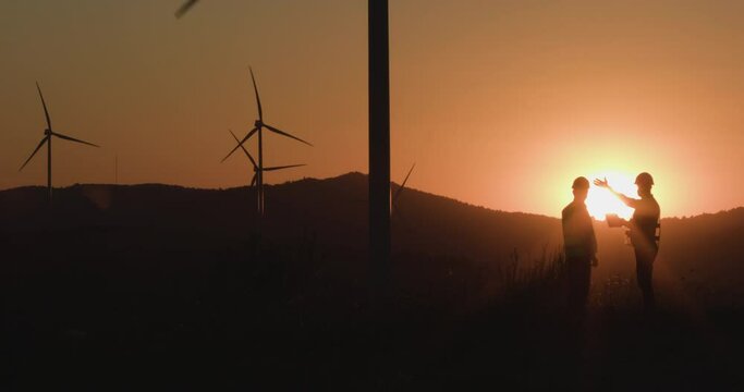Engineers watching information in tablet showing hands on windmills at sunset. Silhouette shooting. The concept of environmentally friendly energy