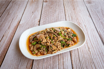 Thai food, spicy minced pork salad (Larb Moo) in white plate on wooden table, popular local food in northeastern Thailand