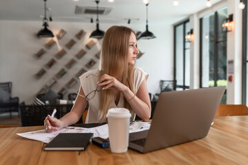 Happy smiling young woman taking a coffee break as she sits at her laptop computer working from a home office