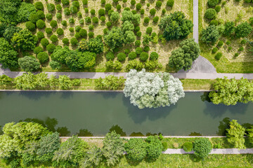 aerial top view of city public park with green lawns, trees and footpaths near water canal in summer time