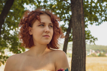 red-haired curly-haired girl in a summer dress posing in the village . High quality photo