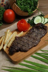 Grilled steak with french fries and vegetables served on wooden board