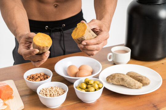 cropped image of muscular man without clothes hold sweet potatoes showing healthy food menu on the table facing forward on isolated background