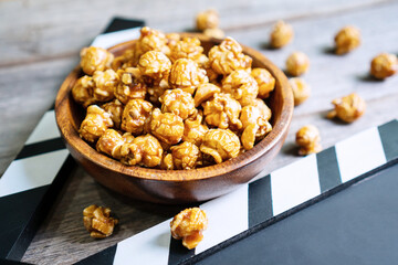 Flat lay of tasty caramel popcorn and clapperboard on wooden table, close up. Movie time concept
