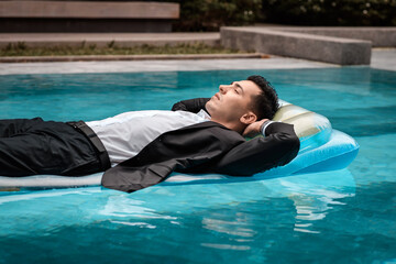 a man in a suit is resting in the pool on an inflatable blue mattress