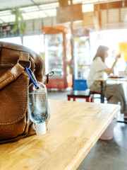 Mini portable alcohol gel bottle to kill Corona Virus(Covid-19) hang on a leather shoulder bag of a woman on table at cafeteria. New normal lifestyle.Selective focus on alcohol gel