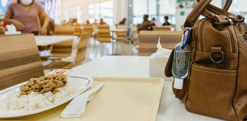 Mini portable alcohol gel bottle to kill Corona Virus(Covid-19) hang on a leather shoulder bag of a woman on table at cafeteria. New normal lifestyle.Selective focus on alcohol gel