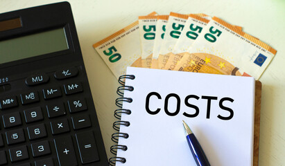 COSTS word in a notebook against the background of calculitar and banknotes