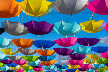Fototapeta na wymiar Colorful vibrant umbrellas hanging over the walking street for a festival on a blue sky sunny day.