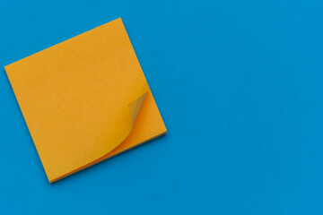 Bright orange posted note on bright blue flat lay background for education or business organization and reminder concepts.