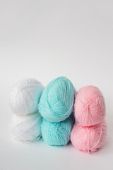 acrylic soft pastel pink, azure and white colored wool yarn thread skeins row on white background, side view, vertical stock photo image with copy space for text