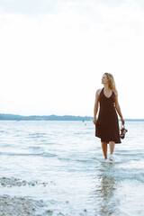 woman in black light dress walking barefoot by sea beach