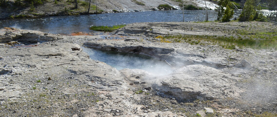 Late Spring in Yellowstone National Park: Spiteful Geyser and Fan Geyser of the Morning Glory Group on the Bank of Firehole River in Upper Geyser Basin