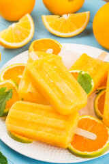 Homemade frosty popsicles with oranges on a blue wooden background