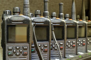 Black walkie talkies lined up in a row sitting upright on charging stations with focus on...