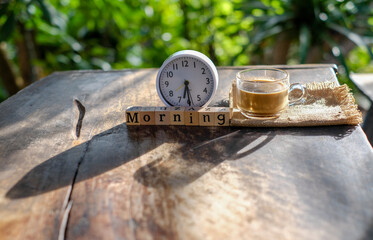 Phrase morning on wooden blocks with white alarm clock and glass of coffee im morning light,...