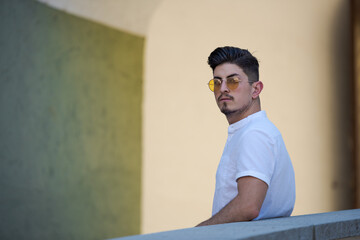 Young styled arabic man with black hair and goatee in white shirt and sunglasses standing in alley...