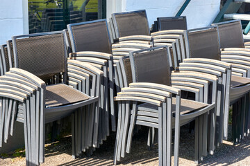 Stacked grey metal chairs with wooden armrests on the terrace of a closed restaurant. 