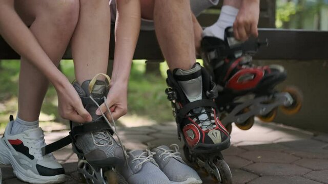 man and woman put on roller skates on their feet while sitting on park bench close-up. friends are going to roller skate.