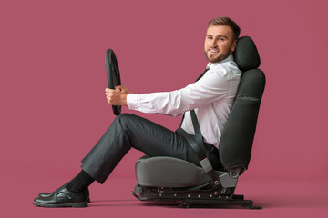 Young businessman with steering wheel sitting on car seat against color background