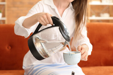 Fototapeta na wymiar Woman pouring hot boiled water from electric kettle into cup at home