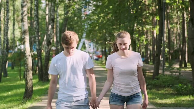 Happy young couple of teenagers rollerblading in park holding hands.