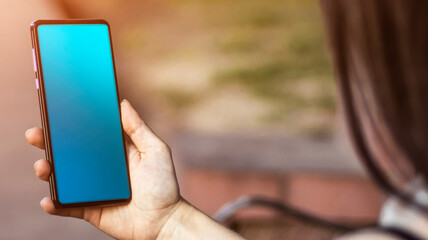 A brunette girl is sitting in the park, holding a mobile phone in her hands. Sunlight, blurred background. lifestyle.