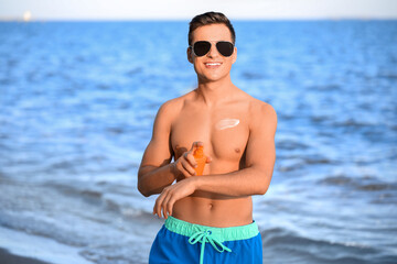 Handsome young man applying sunscreen cream on sea beach