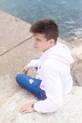 Young pensive teenager male sitting on breakwaters while looking at camera