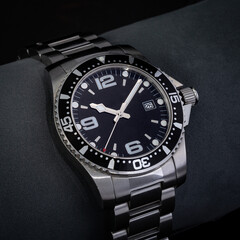 Watch in a studio shot with highly controlled lighting. The watch is used and  has a black dial and steel bracelet.