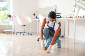 Female makeup artist applying a marking tape on floor in salon during coronavirus epidemic