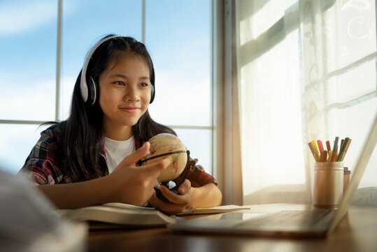 Asian Female Student Using Laptop Computer At Home Learning Geography With Teacher. Studying Through Online E-learning System, Education, Homeschooling And Distance Learning With Internet Online.