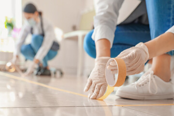 Female makeup artist applying a marking tape on floor in salon during coronavirus epidemic