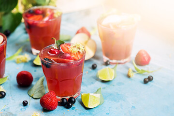 Red cocktails with strawberry, currant and apples in sunlight