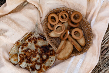 An edible composition of flour baking in a basket on a bedspread, among Golden ears of barley in nature. A big fat donut, vanilla crackers and bagels round