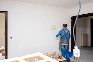 Rear view of female architect woman testing light paint on the renovated wide room wall during the general reconstruction of her dream house