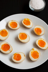 Homemade Unami Soy Sauce Eggs on a white plate on a black surface, side view.