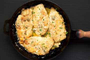 Homemade Italian Chicken Piccata in a cast iron pan on a black background, top view. Flat lay, overhead, from above.