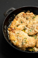Homemade Italian Chicken Piccata in a cast iron pan on a black surface, low angle view. Close-up.