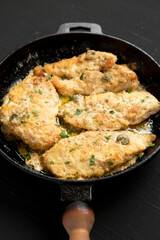 Homemade Italian Chicken Piccata in a cast iron pan on a black background, low angle view.