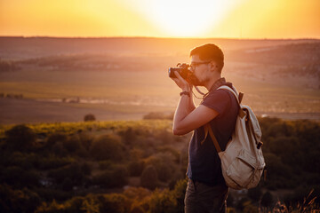 Man photographer with backpack and camera taking photo of sunset mountains