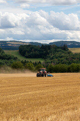 red tractor pulling a blue field cultivator across a harvested wheat field