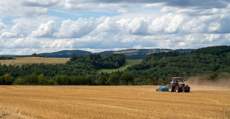 red tractor pulling a blue field cultivator across a harvested wheat field