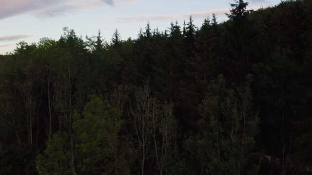 Unveiling drone shot from behind a forest discovering a little town at the swabian alb catching the last sunny moments of a beautiful summer day, germany