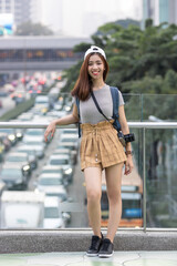 Cheerful young Asian woman tourist raising hands in urban city. Travel and vacation concept.