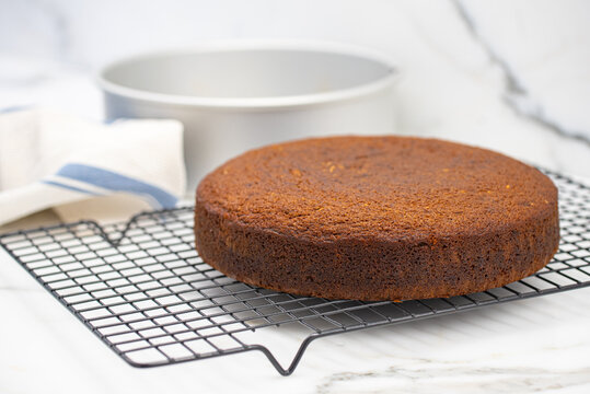 Homemade freshly baked cake cooling on wire rack with round cake pan in background, selective focus