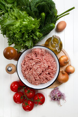 Fresh turkey mince, tomatoes, onions, garlic, herbs, cucumbers, egg, olive oil, salt and pepper on a table