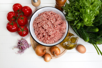 Fresh turkey mince, tomatoes, onions, garlic, herbs, cucumbers, egg, olive oil, salt and pepper on a table
