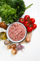 Fresh turkey mince, tomatoes, onions, garlic, herbs, cucumbers, egg, olive oil, salt and pepper on a table
